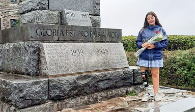 Une adolescente amputée d’une jambe est debout à côté d’un monument commémoratif et tient une rose blanche.