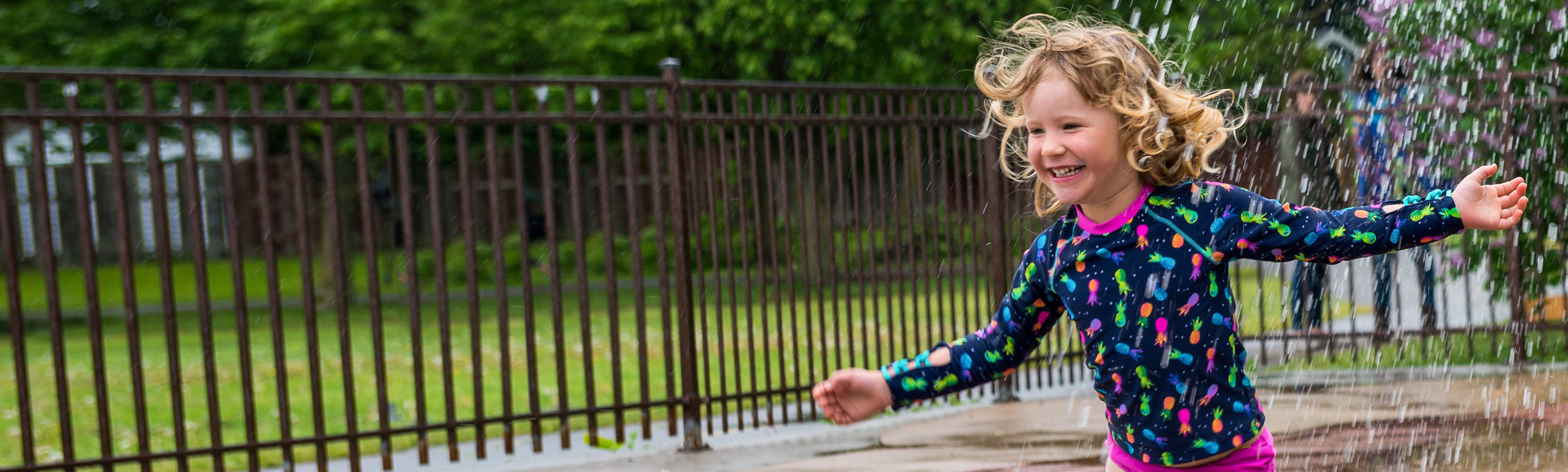 Une enfant amputée souriante s’amuse dans les jeux d’eau. Donnez maintenant.