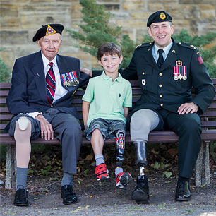 A young boy wearing his artificial leg sitting on a  bench between two war amputee veterans.