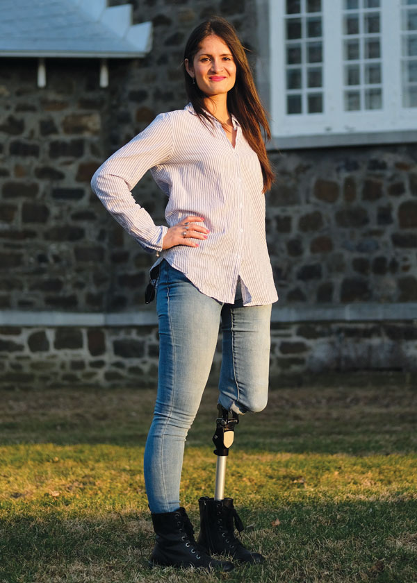 A female adult leg amputee stands in front of a brick building.