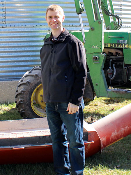 Un homme qui a une désarticulation de l’épaule se tient devant une vis à grain et un tracteur.