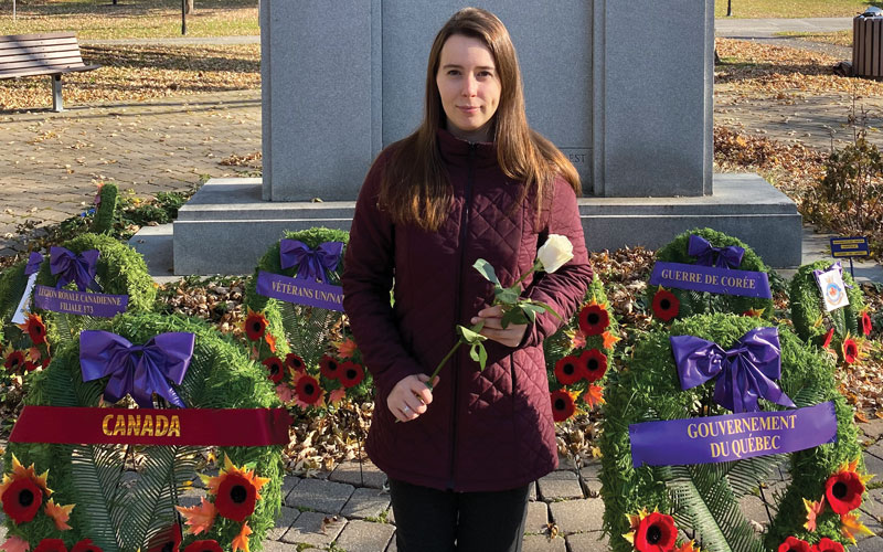 Une jeune femme amputée tient une rose blanche devant un cénotaphe.