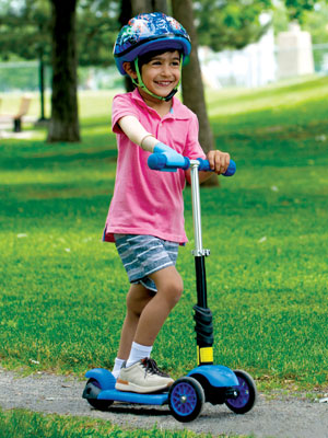 Un jeune garçon amputé d’un bras fait de la trottinette sur le sentier d’un parc.