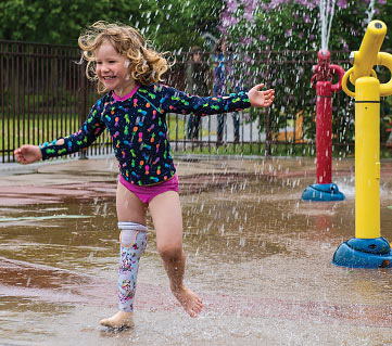 Child amputee Jeanne wearing her water leg while playing at a splash pad.