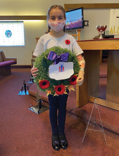 Une enfant amputée d’un bras, portant un masque de protection en tissu, tient une couronne du jour du Souvenir.