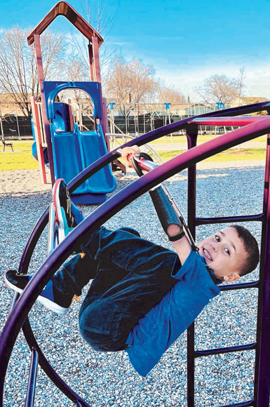 Abel, a young left arm amputee, wears a prosthetic arm with a hook attachment to hang on the monkey bars at a park.