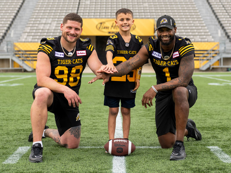 Two male football players kneeling on one knee huddling with a young male arm amputee.