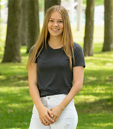 Daphnée, an arm amputee, smiles while standing in front of several trees.