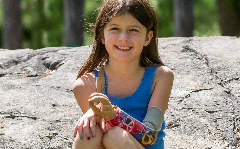 Sophia, an arm amputee, sitting on a large rock. See Sophia’s Story.