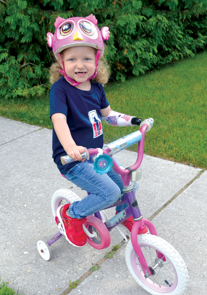 Une jeune fille amputée fait du vélo à l’aide de son bras artificiel et d’un dispositif fixé sur le guidon.